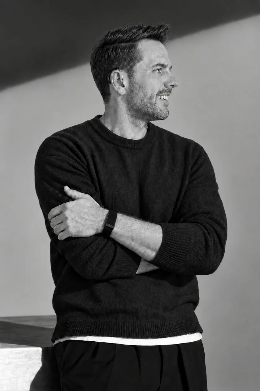 Nicholas Scarcliffe in profile, arms folded and smiling, his hearing aid visible behind his ear